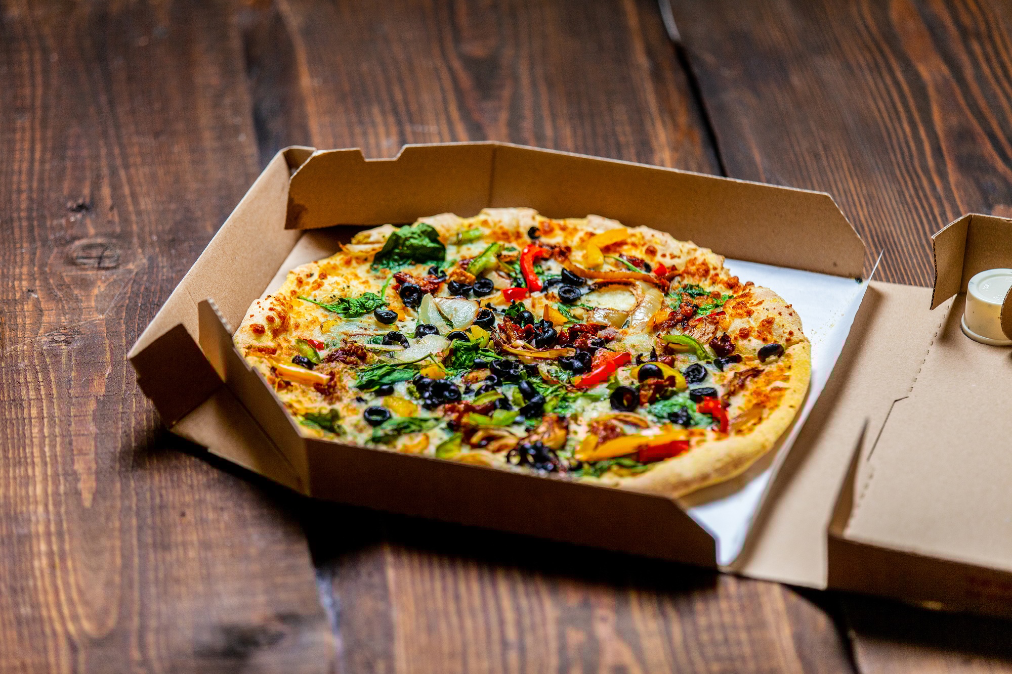 mediterranean Pizza with olives and cheese in cardboard on wooden table