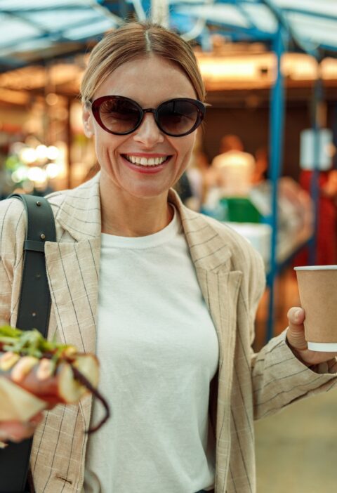 Smiling woman tourist is having a takeaway fast food lunch on food market and drink