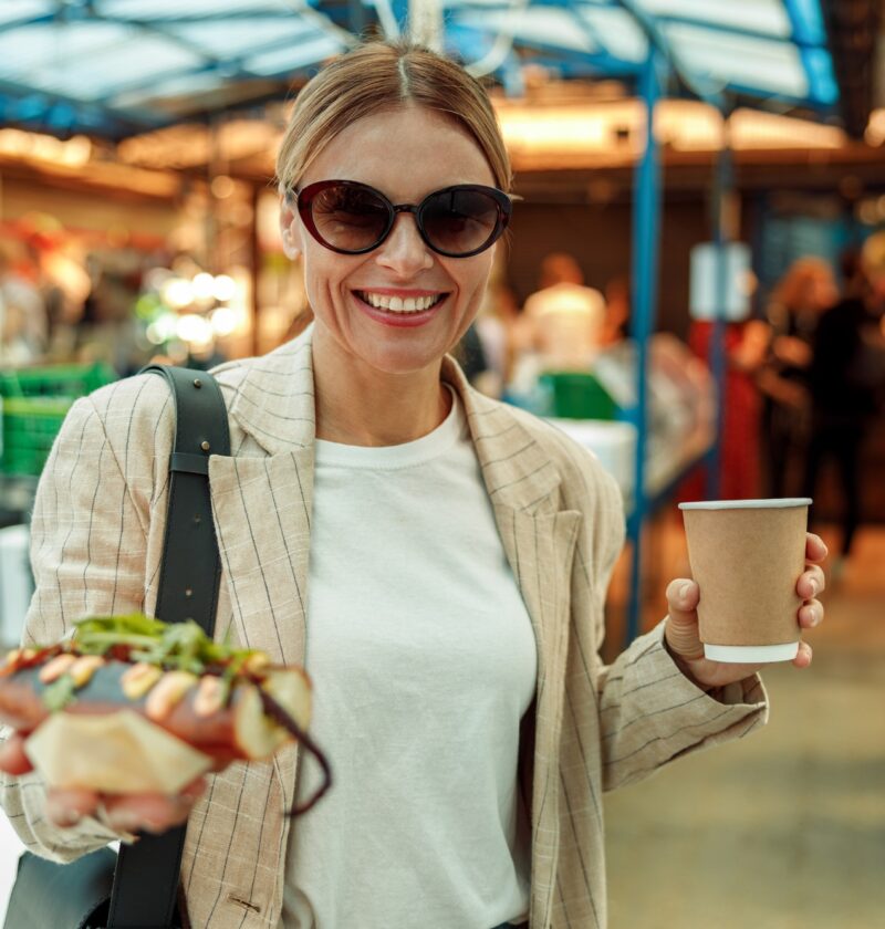 Smiling woman tourist is having a takeaway fast food lunch on food market and drink