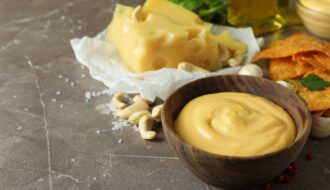 Bowls with cheese sauce and ingredients on gray textured table