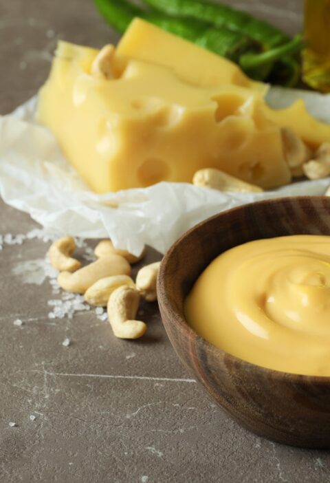 Bowls with cheese sauce and ingredients on gray textured table