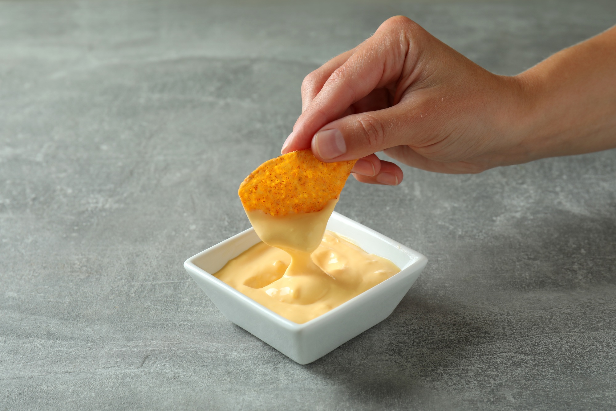 Female hand dips chip in cheese sauce, close up