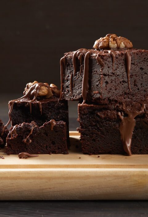 Stack of baked square pieces of chocolate brownie cake on brown wooden cutting board