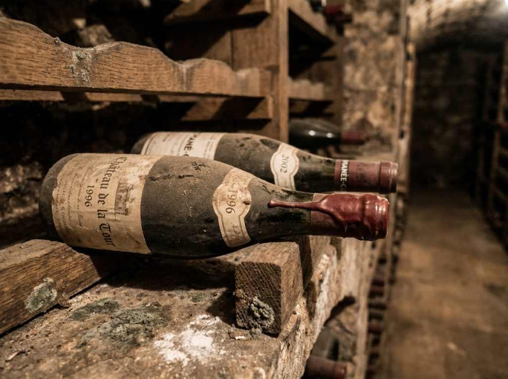 Bouteilles de vins de garde bourguignons poussiéreux sur des pupitres en chêne dans une cave historique de Bourgogne